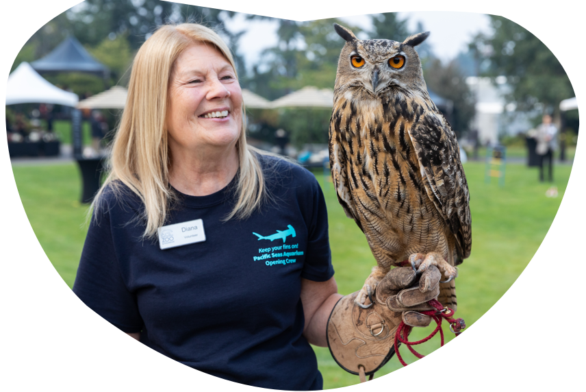 A zookeeper smiles while holding an owl on her arm.