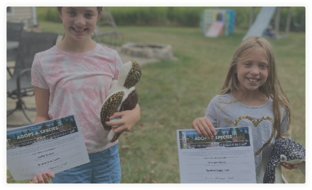 Two girls hold paperwork from the Point Defiance Zoo Society while smiling.